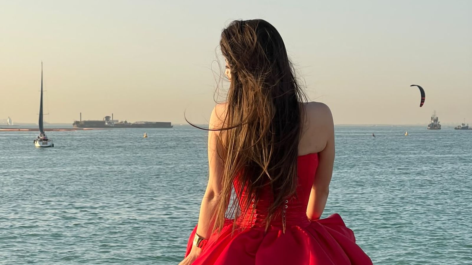 Liliia in a red dress sitting on rocks by the sea